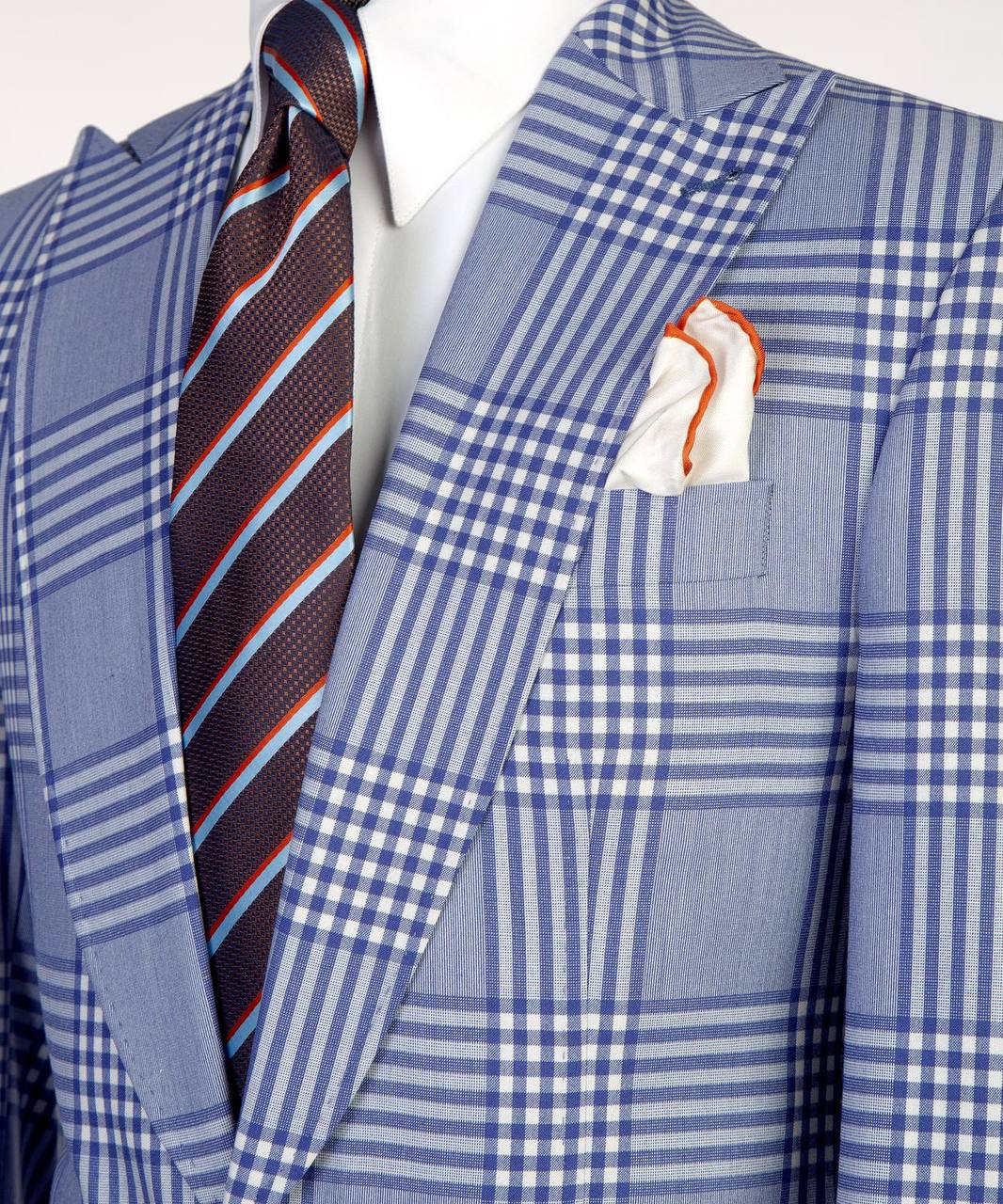 Close-up of light blue plaid suit jacket styled with white shirt, striped tie, and pocket square.